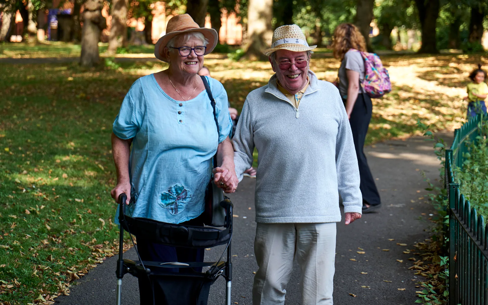 Ouder koppel dat samen door een groen park wandelt, de vrouw met een rollator